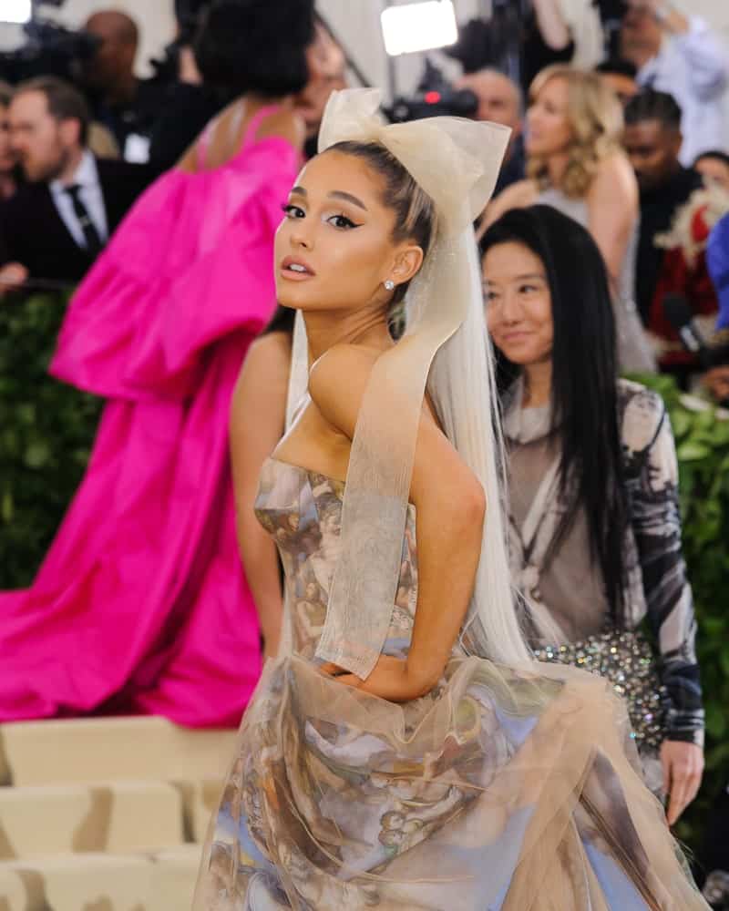 Ariana Grande complements her ponytail hairstyle with a dramatic long organza bow during the 2018 Metropolitan Museum of Art Costume Institute Benefit Gala on May 7, 2018. She finished the look with a glamorous floral dress and stud earrings.