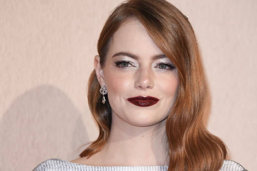 On October 18, 2018, Emma Stone was at the London Film Festival screening of "The Favourite" at the BFI South Bank, London. She flaunted her lovely lips with some dark make-up and a pinned side-swept hairstyle with waves.