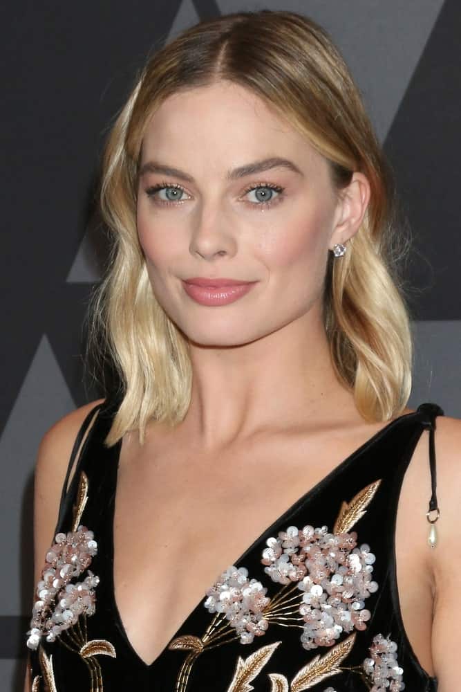 Margot Robbie in a black floral dress during the AMPAS 9th Annual Governors Awards at Dolby Ballroom on November 11, 2017. She paired it with a center-parted wavy hairstyle that's defined with blonde highlights.