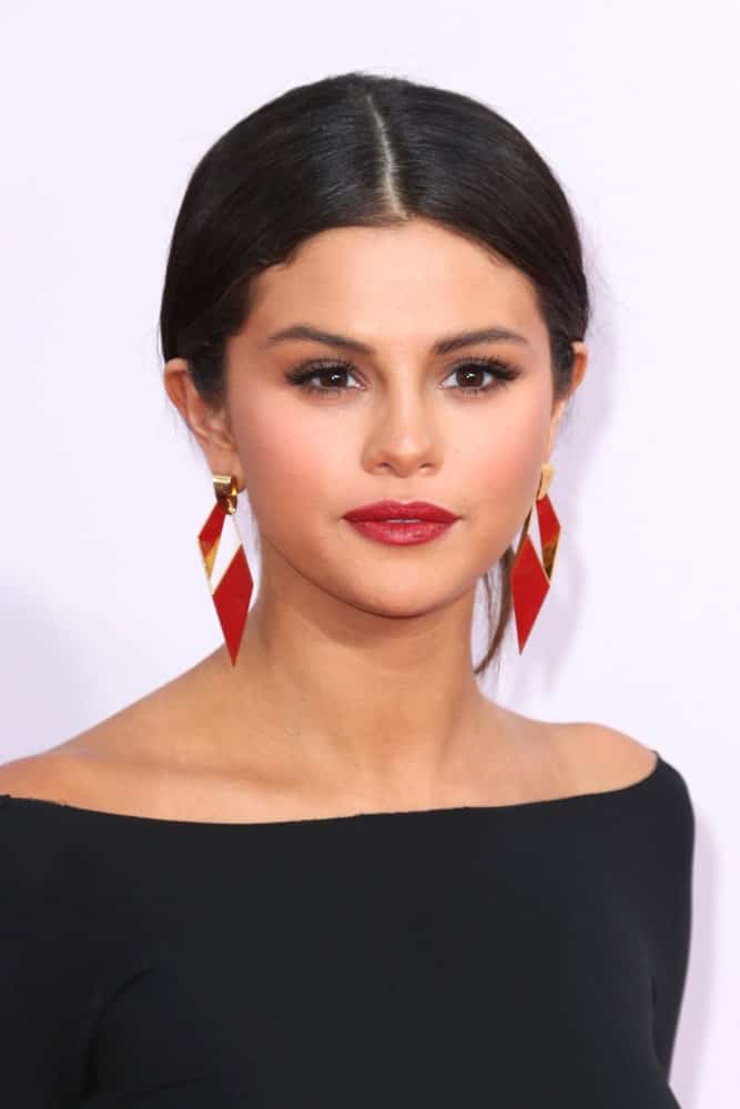 Selena Gomez wore a neat loose bun hairstyle with a simple black outfit and red earrings at the 2014 American Music Awards - Arrivals at the Nokia Theater on November 23, 2014 in Los Angeles, CA.