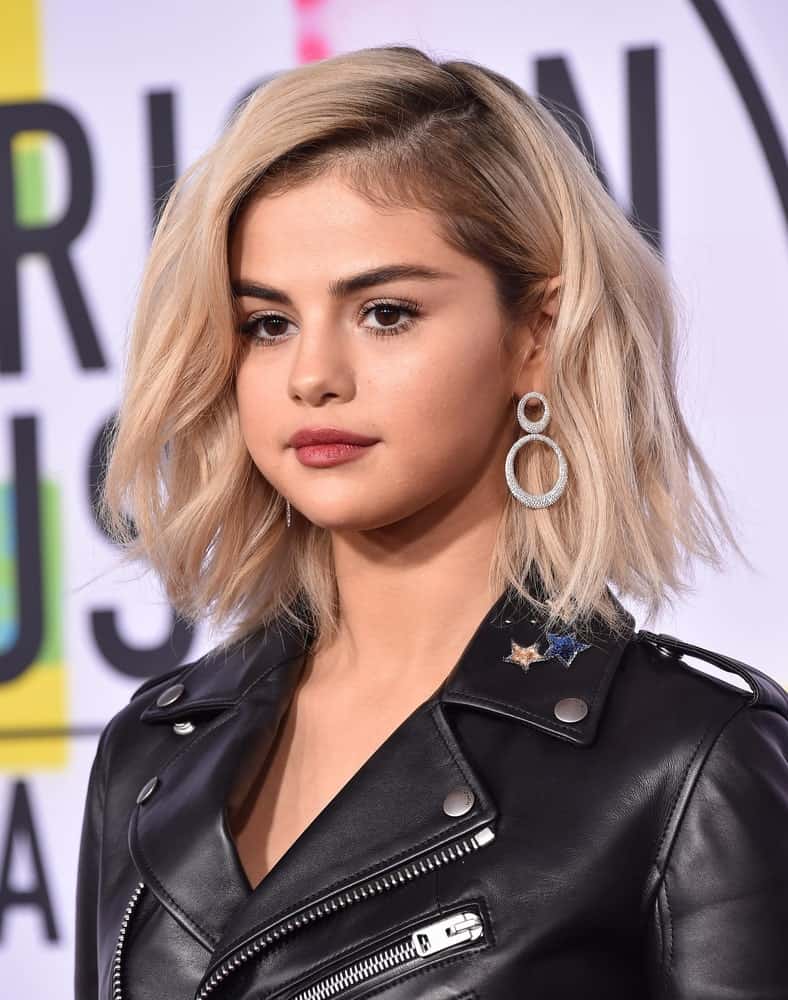 Selena Gomez attended the 2017 American Music Awards on November 19, 2017 in Los Angeles, CA. She paired her cool black leather jacket with a short tousled and wavy platinum blonde hairstyle.