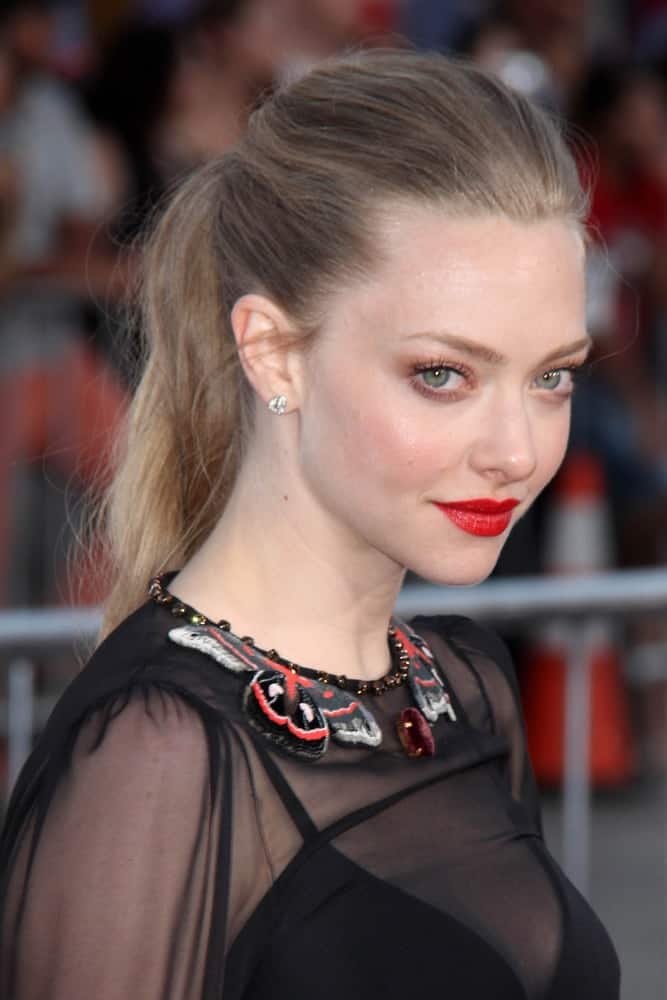 Amanda Seyfried's sheer black outfit and bold red lips are complemented by her lovely messy ponytail hairstyle with a slight tousle at the "A Million Ways To Die In The West" World Premiere at Village Theater on May 15, 2014 in Westwood, CA.