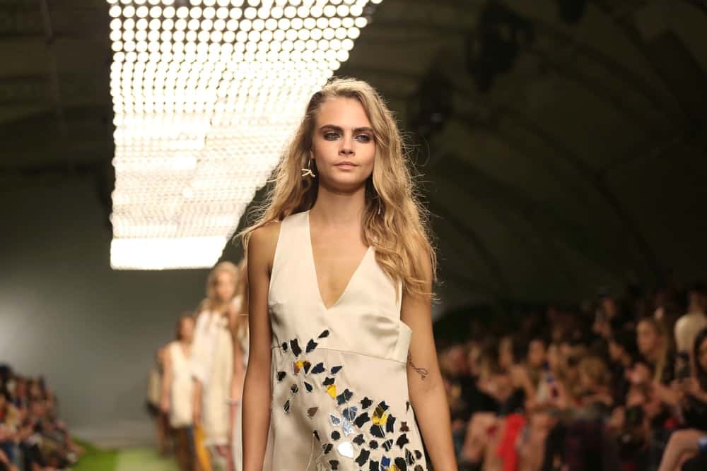 Cara Delevingnewas dressed in a beautiful simple white dress to pair with her long, side-swept wavy sandy blond hairstyle at the London Fashion Week SS14 - Topshop Unique - Catwalk in London on September 15, 2013.