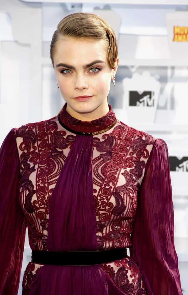 Cara Delevingne went with a slick vintage look to her sandy blond bun hairstyle to go with her red sheer dress at the 2015 MTV Movie Awards held at the Nokia Theatre L.A. Live in Los Angeles, USA on April 12, 2015.