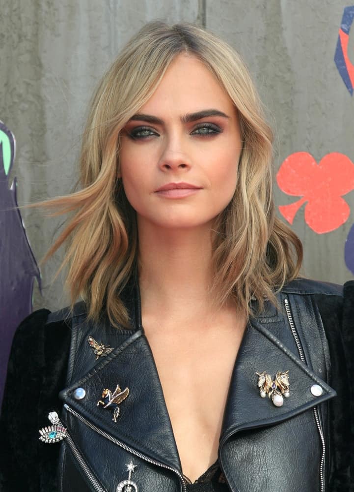 Cara Delevingne was quite cool in her dark gray leather jacket and edgy black outfit to match with her wavy, loose and highlighted sandy blond hairstyle with a slight side-swept finish at the Suicide Squad film premiere on Aug 03, 2016 in London.