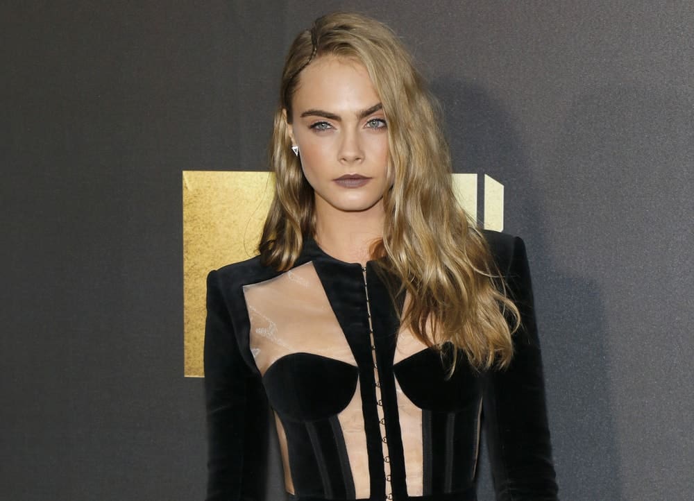 Cara Delevingne wore a fashionable black velvet outfit that complemented her long and wavy highlighted loose hairstyle that has a pinned side-swept finish at the 2016 MTV Movie Awards held at the Warner Bros. Studios in Burbank, USA on April 9, 2016.