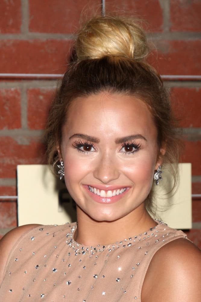 Demi Lovato flashed a brilliant smile to go with her beige dress and messy top knot bun hairstyle that has blond highlights at the FOX Eco-Casino Party 2012 at Bookbindery on September 10, 2012 in Culver City, CA.