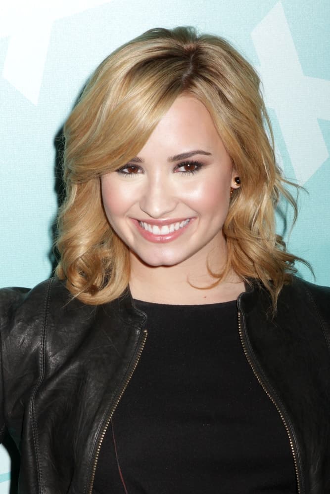 Demi Lovato wore a black outfit and leather jacket with her blond shoulder-length curls with long side-swept bangs and highlights when she attended the 2013 Fox Upfront at Wollman Rink on May 13, 2013 in New York City.