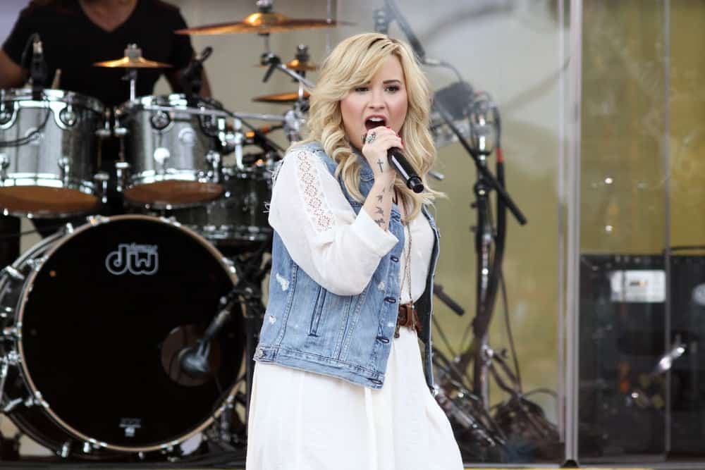 Demi Lovato performed at the 'Good Morning America' concert series in Central Park on June 28, 2013 in New York City. She wore a long white dress with her denim jacket and shoulder-length curly blond hairstyle with long side-swept bangs.