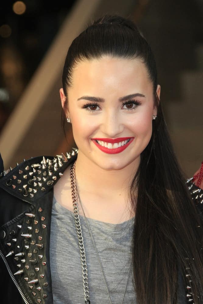 Demi Lovato was at the Topshop Topman LA Grand Opening at The Grove on February 14, 2013 in Los Angeles, California. She paired her casual gray shirt with a cool black leather jacket and a slick and straight raven high ponytail hairstyle.