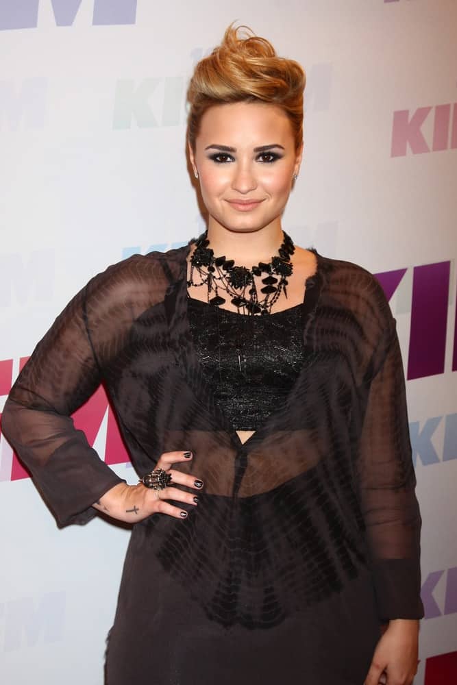 Demi Lovato attended the 2013 Wango Tango concert produced by KIIS-FM at the Home Depot Center on May 11, 2013 in Carson, CA. She dyed her long hair into a sandy blond tone and swept it up for a swirly upstyle that has a slight tousle.