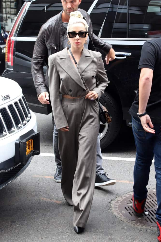 On May 28, 2018, Lady Gaga was seen on a fine New York City day walking the streets wearing a gray pantsuit that she paired with a brown belt, black sunglasses and an elegant top knot hairstyle.