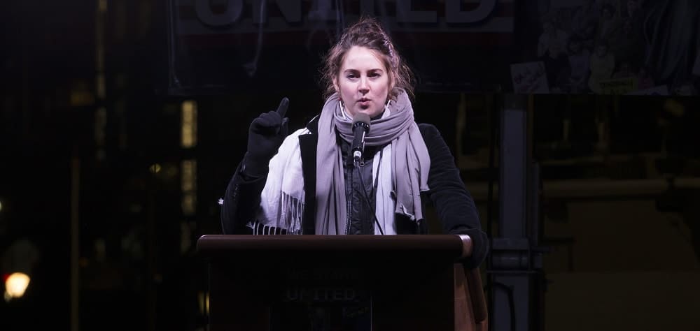 On January, 19 2017, Shailene Woodley spoke onstage during the We Stand United NYC Rally outside Trump International Hotel & Tower. She wore her winter outfit with her makeup-less face and messy bun hairstyle with loose tendrils.