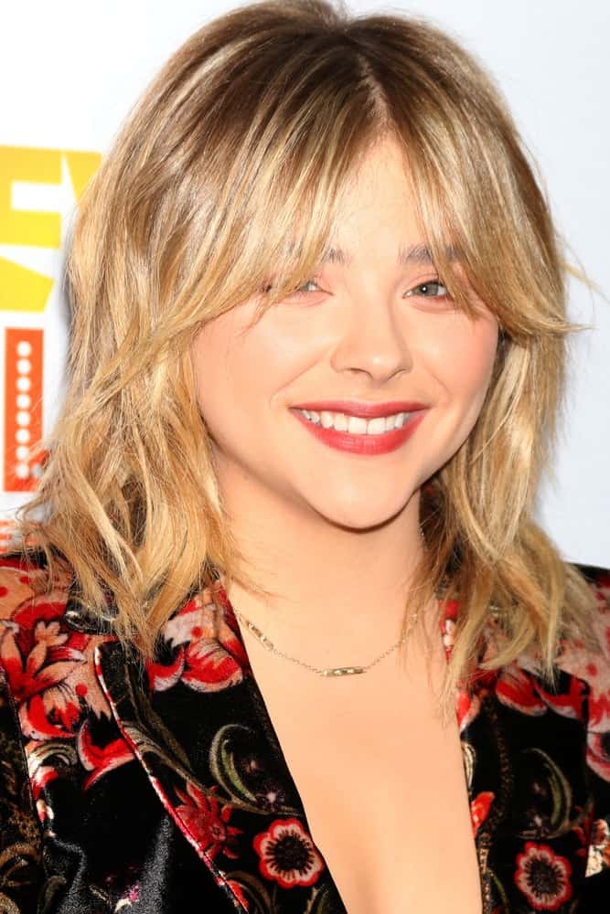 Chloe Grace Moretz was at the TrevorLIVE Los Angeles 2016 at Beverly Hilton Hotel on December 4, 2016 in Beverly Hills, CA. She wore a colorful floral smart casual outfit with her shaggy sandy blonde hairstyle with layers and eye skimmer bangs.