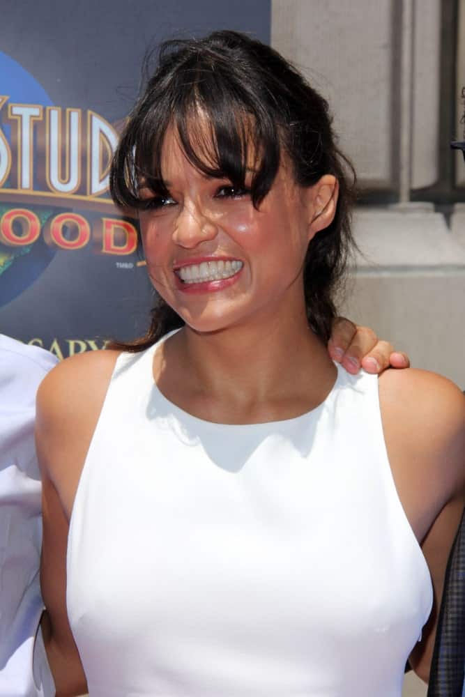 Michelle Rodriguez switched her usual dark wardrobe to a much lighter look by sporting an all-white jumpsuit and had her raven-colored tresses in a ponytail with fringe as she attends the "Fast & Furious - Supercharged" Ride Press Event on June 23, 2015.