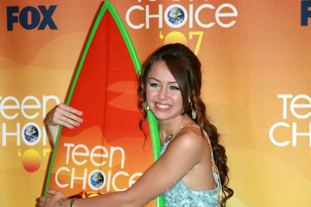 Miley Cyrus posed with the iconic surf board in the press room of the 2007 Teen Choice Awards held at the Gibson Amphitheater in Universal City, CA on August 26, 2007. She was wearing a colorful dress that went well with her classy wavy hairstyle.