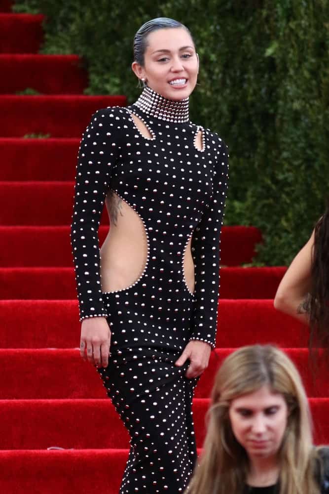 Miley Cyrus attended the Costume Institute benefit gala at the Metropolitan Museum of Art on May 4, 2015 in New York. She wore a lovely long black dress incorporated with metal studs that went well with her slicked back dark pixie hair.