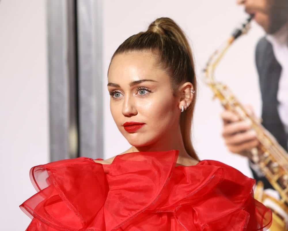 Miley Cyrus was at the "Isn't It Romantic" World Premiere at the Theatre of Ace Hotel on February 11, 2019 in Los Angeles, CA. She was absolutely lovely in her red frilly dress, matching lipstick and slick highlighted high ponytail.