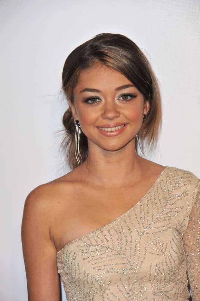 Sarah Hyland was at the 9th Annual Teen Vogue Young Hollywood Party at Paramount Studios, Hollywood on September 23, 2011. She was seen wearing an asymmetrical beige gown paired with a loose and messy low bun hairstyle with long side-swept bangs.
