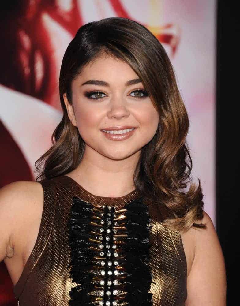 Sarah Hyland attended the "The Hunger Games: Catching Fire" Los Angeles Premiere on November 18, 2013, in Los Angeles, CA. She paired her golden dress with a wavy side-swept hairstyle that has layers and highlights as well as long side-swept bangs.