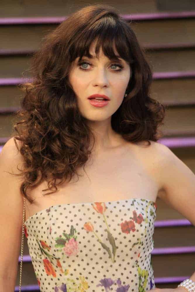 Zooey Deschanel was at the 2014 Vanity Fair Oscar Party on March 2, 2014, in West Hollywood, California. She paired her stunning floral strapless dress with a tousled curly brunette hairstyle with blunt bangs.