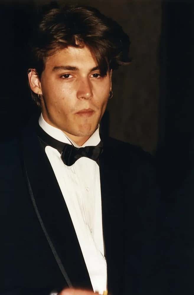 A young Johnny Depp steps out to a celebrity event held in Los Angeles, CA circa 1990 in the typical 90's boy-next-door look that is thick and center parted.