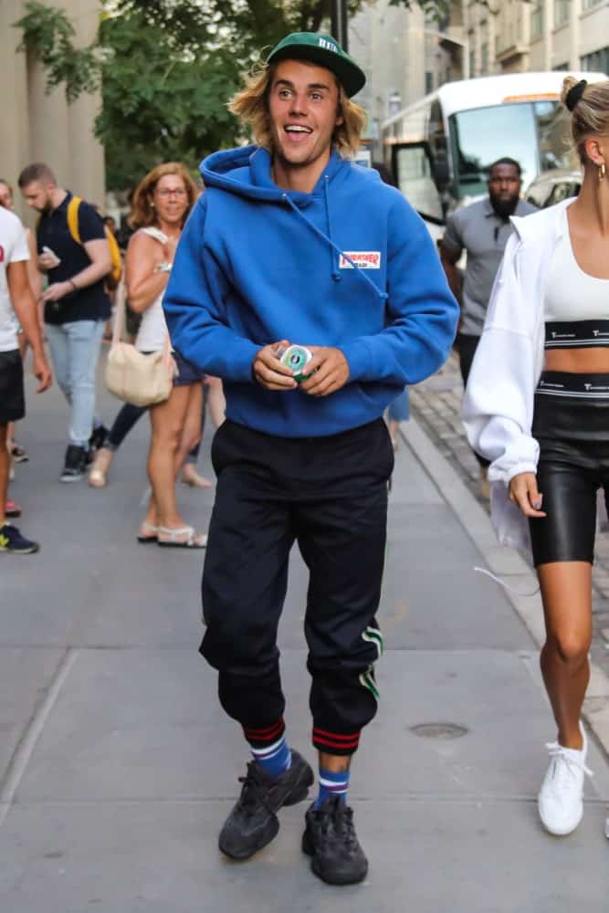 Justin Bieber was spotted in New York City on July 12, 2018 wearing a green cap that complements his long blonde hair. The look was completed with a blue sweatshirt and black jogger pants.