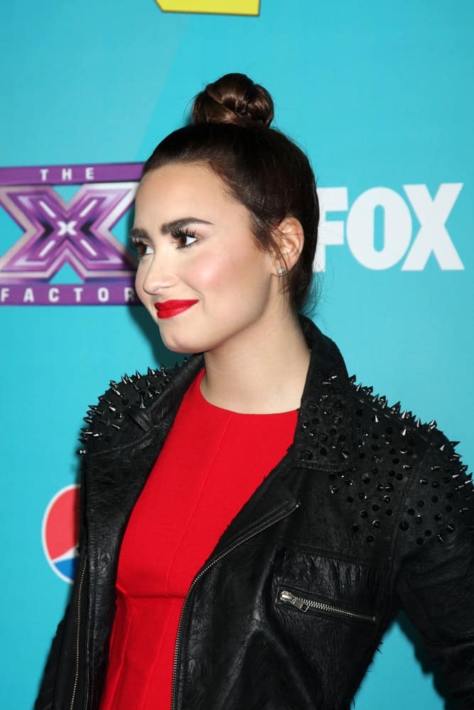 Demi Lovato wore a cool black leather jacket over her red dress to pair with her neat top knot bun hairstyle with some loose tendrils at the X-Factor Season Two Finalist Party at the SLS Hotel at Beverly Hills on November 5, 2012, in Los Angeles, CA.