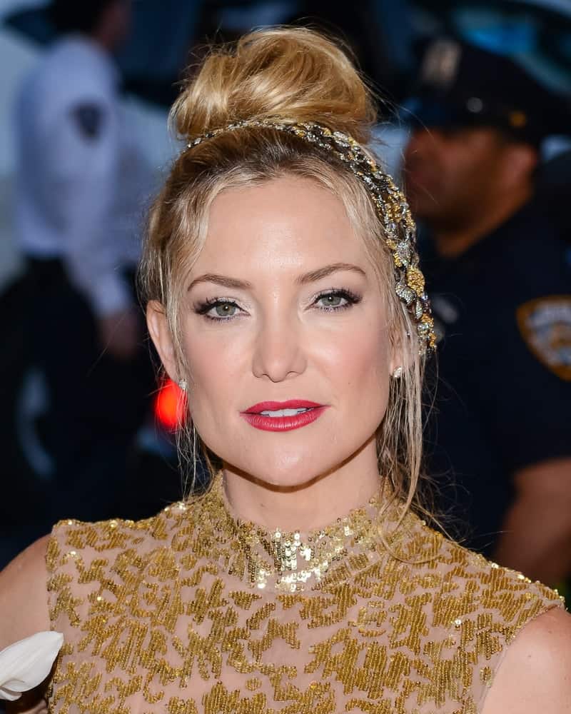On May 04, 2015, Kate Hudson attended the ‘China: Through The Looking Glass’ Costume Institute Gala held at the Metropolitan Museum of Art in New York City, New York. She wore a gold sequined sheer dress with her messy top knot bun hairstyle with loose tendrils.