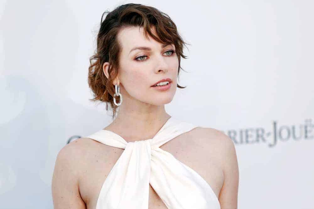 Milla Jovovich attended the amfAR Cannes Gala 2019 at Hotel du Cap-Eden-Roc on May 23, 2019, in Cap d'Antibes, France. She was stunning in a white dress that she paired with a messy dark brunette bun hairstyle that has side-swept bangs.