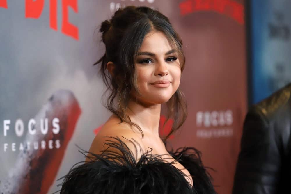 Selena Gomez emphasized her youthful glow with her lovely black dress and messy half up bun with loose tendrils and bangs at the premiere of “The Dead Don’t Die” at the Museum of Modern Art on June 10, 2019, in New York City.