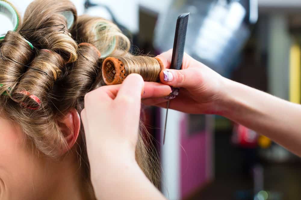 stylist putting in hair rollers in woman's hair.