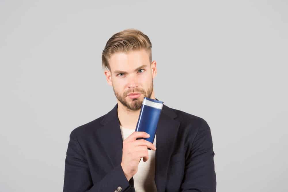 Man with a slick hairstyle holding an anti-dandruff shampoo.