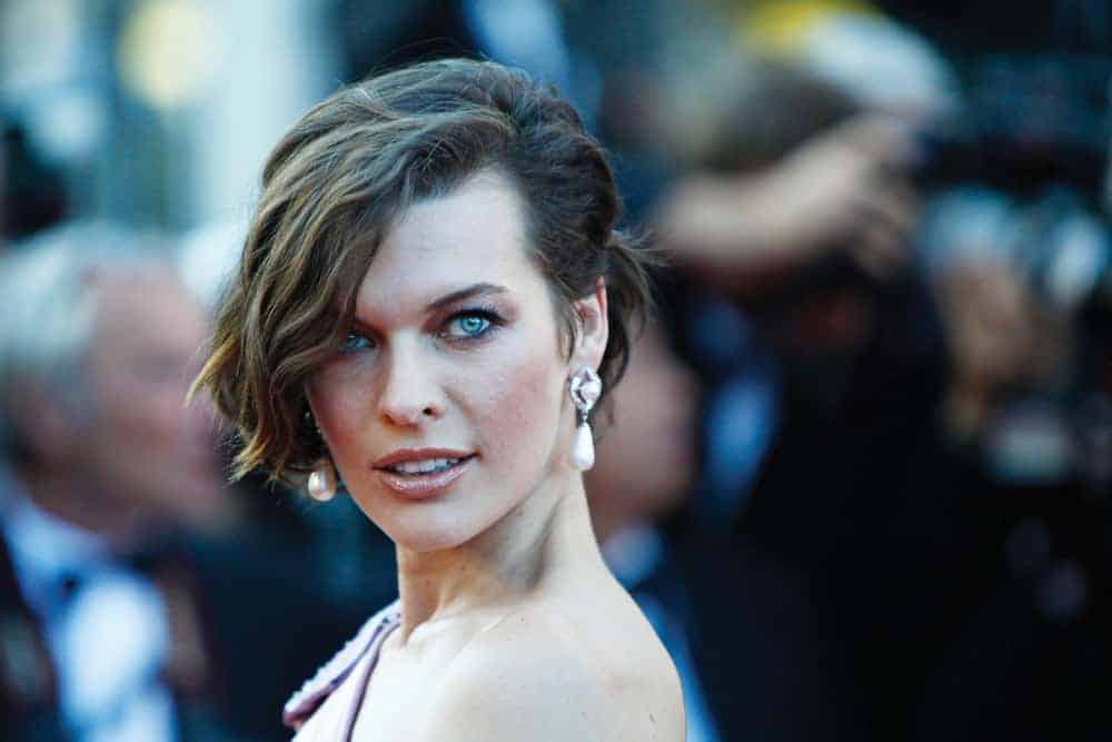 Mila Jovovich attended the 'On The Road' Premiere at Palais des Festivals on May 23, 2012, in Cannes, France. She was quite elegant in her pink dress and brunette bun hairstyle that has loose, side-swept, and highlighted bangs.