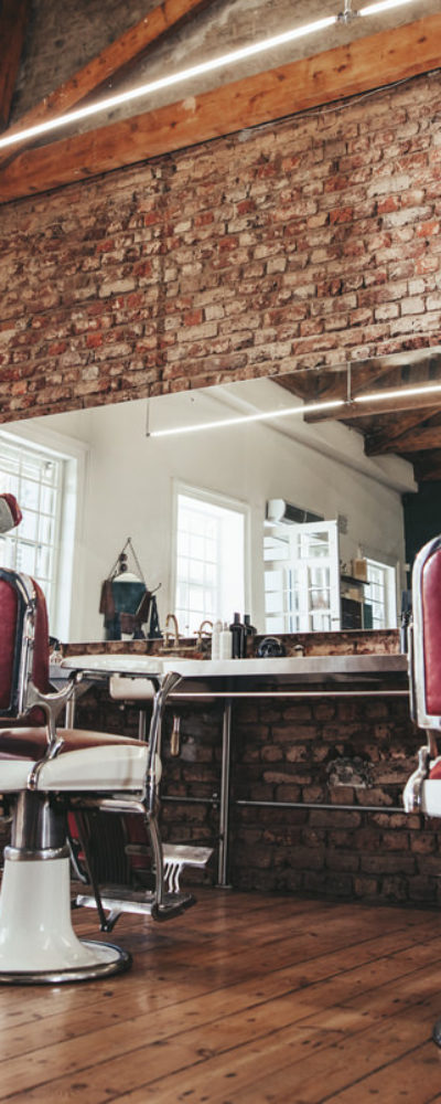 Stunning barber shop interior with tall ceiling, brick wall, old school chairs and wood floor.