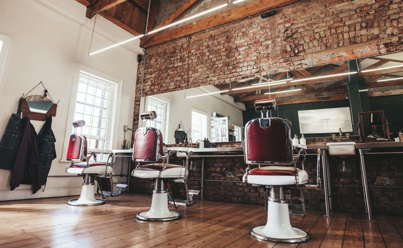 Stunning barber shop interior with tall ceiling, brick wall, old school chairs and wood floor.