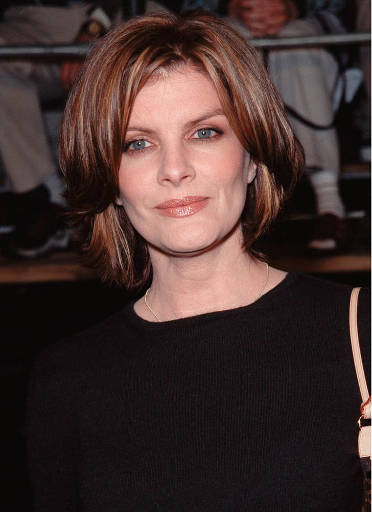 The next hairstyle is portrayed by Rene Russo. Her hairstyle is a mid-length cut that is beautified with auburn and brown-color highlights in order to add dimension to the look of the style. In addition to this multi-dimensional color, the hair is curled towards the back of the face, but the longer, front sections of the hair rest just lightly on Russo’s forehead for style purposes. 