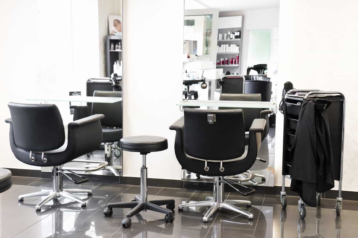 Mirrors that cover almost all of the wall expands the space in this salon. The white walls and glossy light grey floors are complimented by the black and stainless steel chairs. Grey shelves highlight the bright red of the product packaging. 