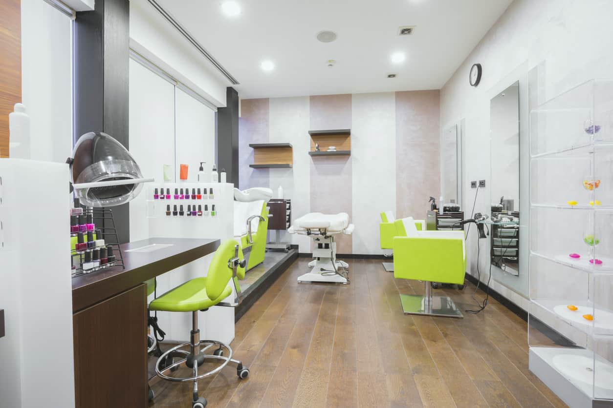 Neon yellow-green pops in this white and grey salon. Natural wood floors and accents and a striped accent wall make this Modern salon feels earthy and sophisticated, and the bright colors of the nail polish really stand out against the background. The soft glow of the lights is reflected by the large mirrors and stainless steel bases of the bright chairs. 