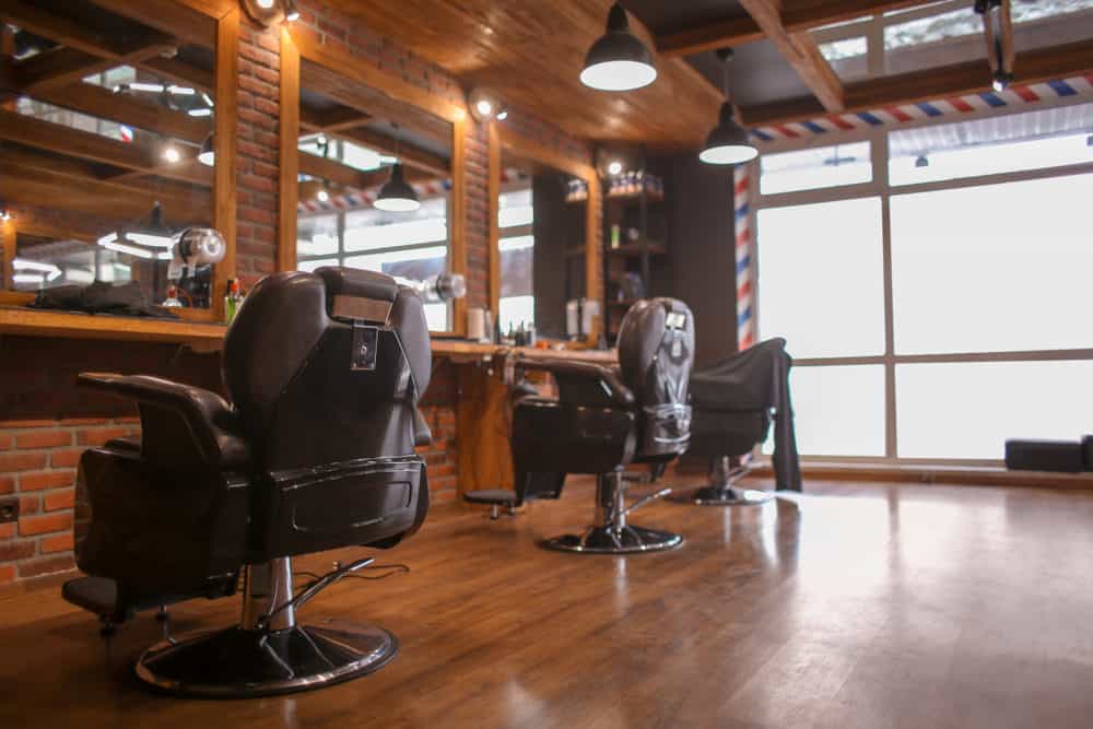 Warm brick walls and oak ceiling and floors with a hint of gloss create a warm and inviting environment. The famous barber pattern frames the large window, and the dark brown buttery leather chairs complement the vintage look of the hanging metal pendant lights. 