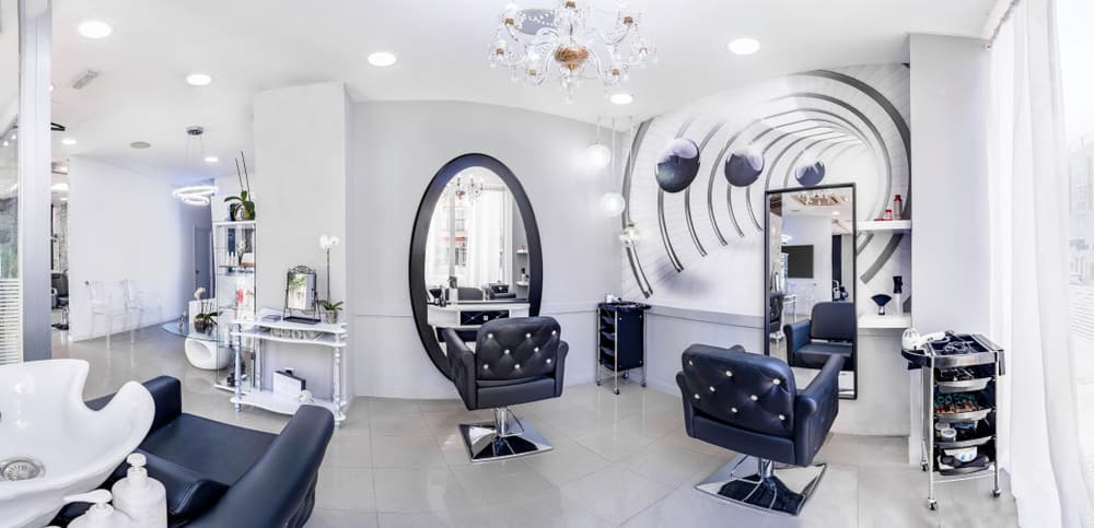 The gold and crystal chandelier draws the eye up to the ceiling, and numerous canister lights add a soft glow to the room. The futuristic mural on the wall behind one of the mirrors makes it seem as if the room goes on further and the black and white buttoned leather chairs look comfortable as well as stylish. 