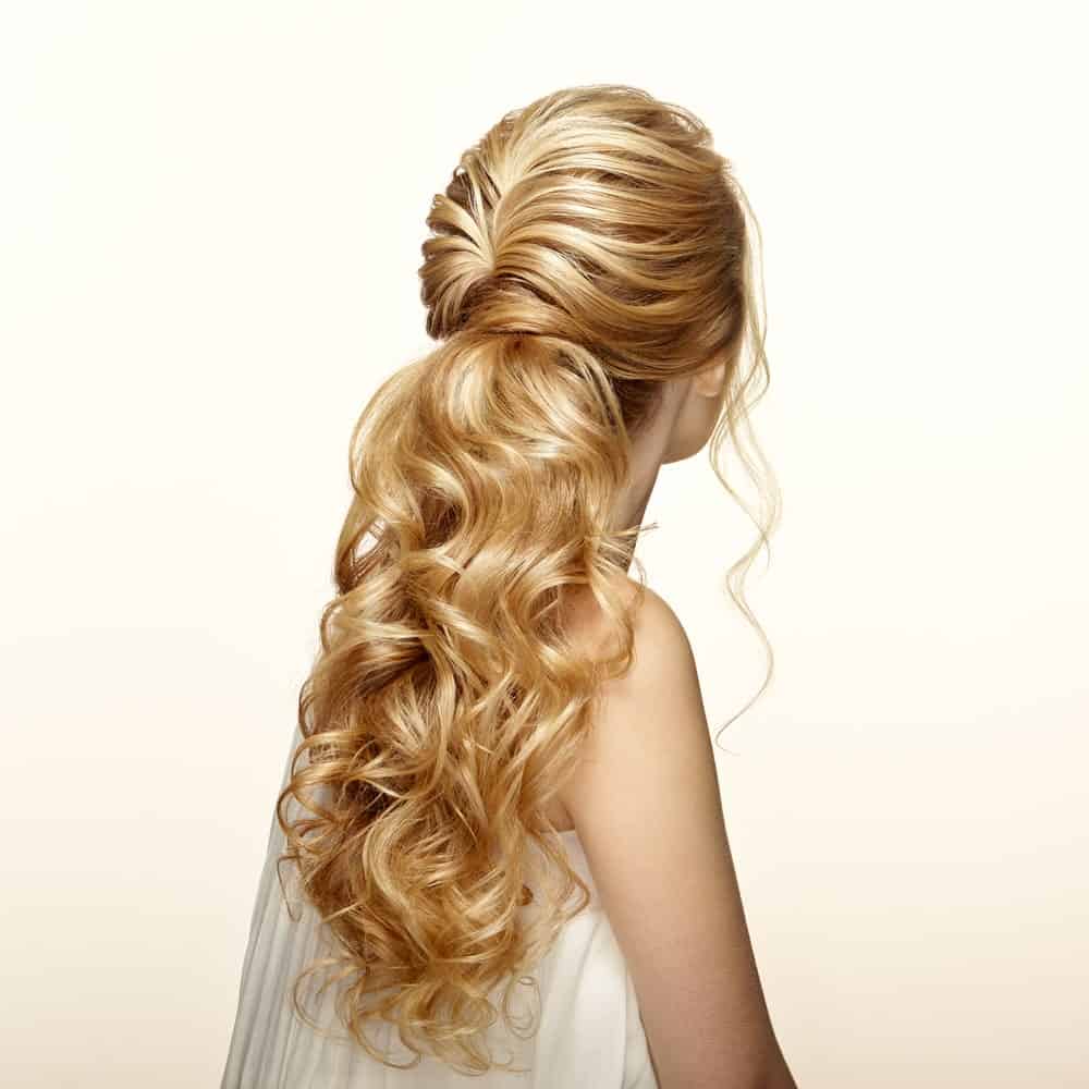 This half up, half down hairdo combines soft waves for the pinned top half of the hair with softly bunched curls on the bottom half for an intricate but beautiful hairdo. There is slight backcombing at the top to give some lift and volume to the hair and hold the waves in place. This is best done on longer hair so there is more space to play with it. 