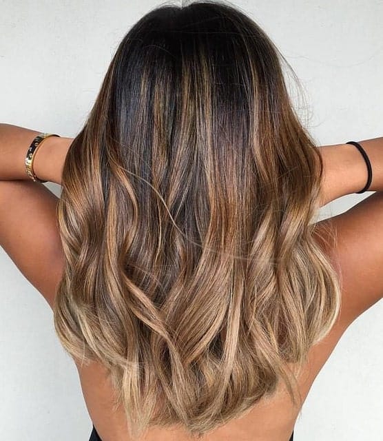 This balayage is made up of chestnut, caramel brown, sandy blond and ash blond shades. With her tanned skin, the highlights look like they have been naturally bleached by the sun.