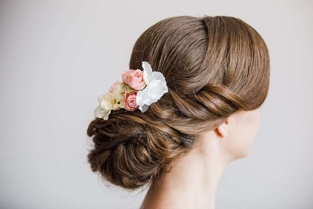 A side bun with flowers is never going to look bad. This particular hairstyle uses elegantly swept bangs with soft curling twists to complete the look. 