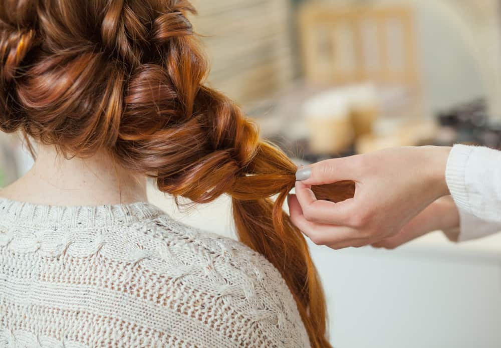 A woman styling a messy French braid on a redhead