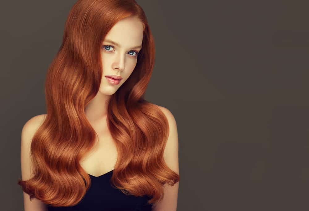 A young woman with long wavy auburn hair on a dark background