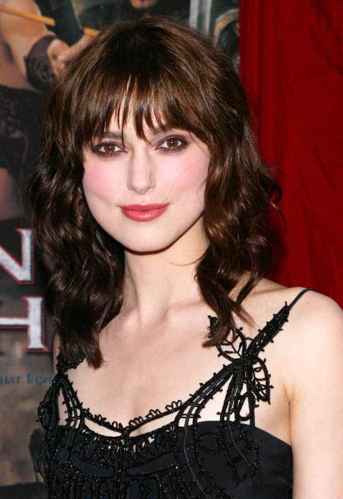 Actress Keira Knightley was at the world premiere of King Arthur at the Ziegfeld Theater on June 28th, 2004 in New York City. She wore a stunning black dress with her shoulder-length dark wavy hairstyle that has wispy layered bangs.