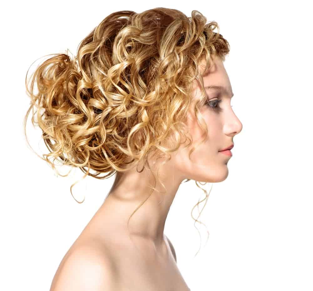 This hairstyle is the perfect messy look that will leave you looking chic and trendy. The hairstyle features a low hanging messy bun at the back of the head coupled with loose strands of hair falling around the face. It is the ideal hairstyle for all the busy bees out there who cannot spare more than a few minutes for styling up their gorgeous long and blonde curly hair. To recreate this look make sure that your bun is loosely tied, putting the power of your curls to full use. 