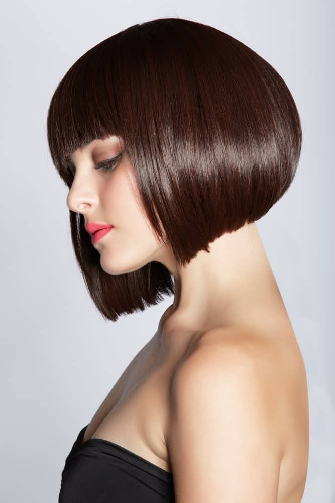 This is a classic, funky brunette angled bob with thick fringe-bangs in the front. The hair is super voluminous from the back and appears to be a little poofed up, giving the hair a very modern, trendy touch.