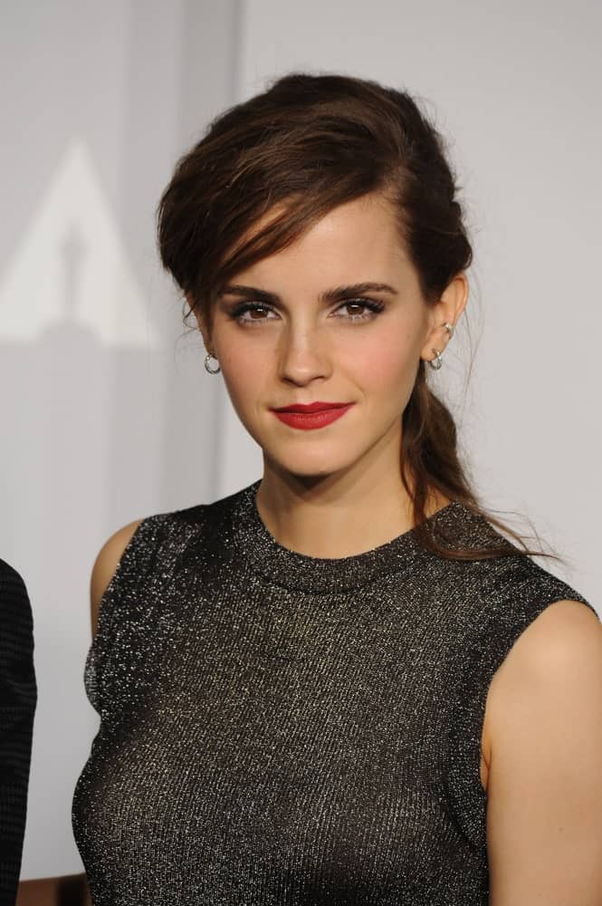 Emma Watson has swept her bangs to the side in a messy way. This pairs well with her perfect earrings, red lips, and fierce eye makeup perfectly. The rest of her hair is tied back in an untidy pony, which actually compliments her outfit and makeup in the best way possible. This look will definitely make you look effortless as well. 